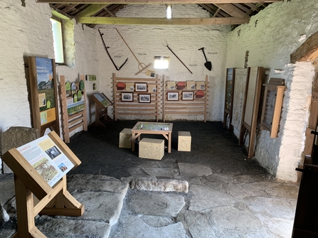 Inside Hannah's Meadow old barn with interpretation sign panels around the edge and old hay meadow tools on wall in background