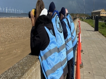 group of people wearing blue 'little tern warden' vests watching beach through binoculars