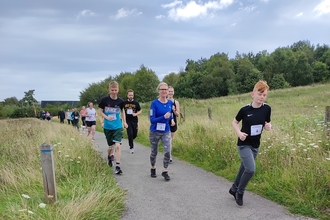 group of people running along path with grassland on either side