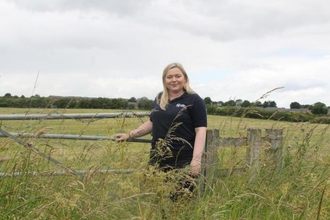 Woman standing next to gated entrance to fields