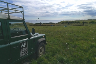 Landrover parked near meadow with coast in background