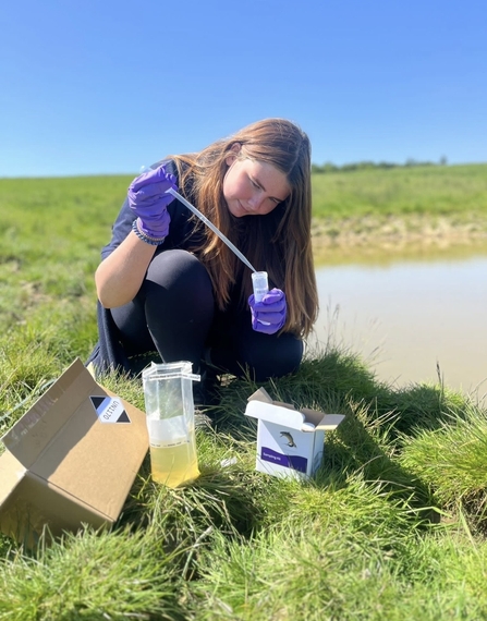 Woman next to pond with pipette and test tube from eDNA testing kit