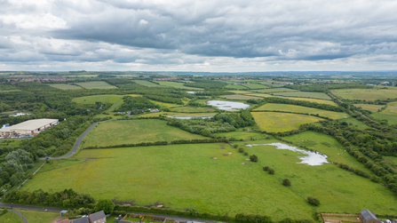 Overhead photo showing fields with nature reserve, including woodland and ponds, in distance