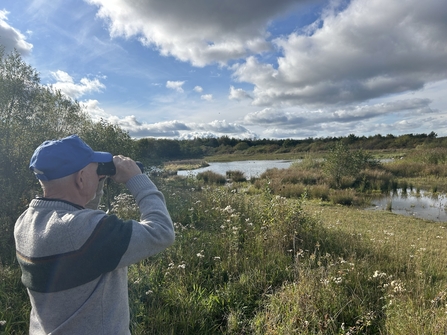 man wearing cap and holding binoculars looking out over ponds