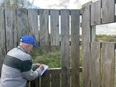 man wearing cap and holding notepad and pen at bird screen