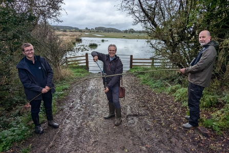 Three men in front of wetland cutting willow branch